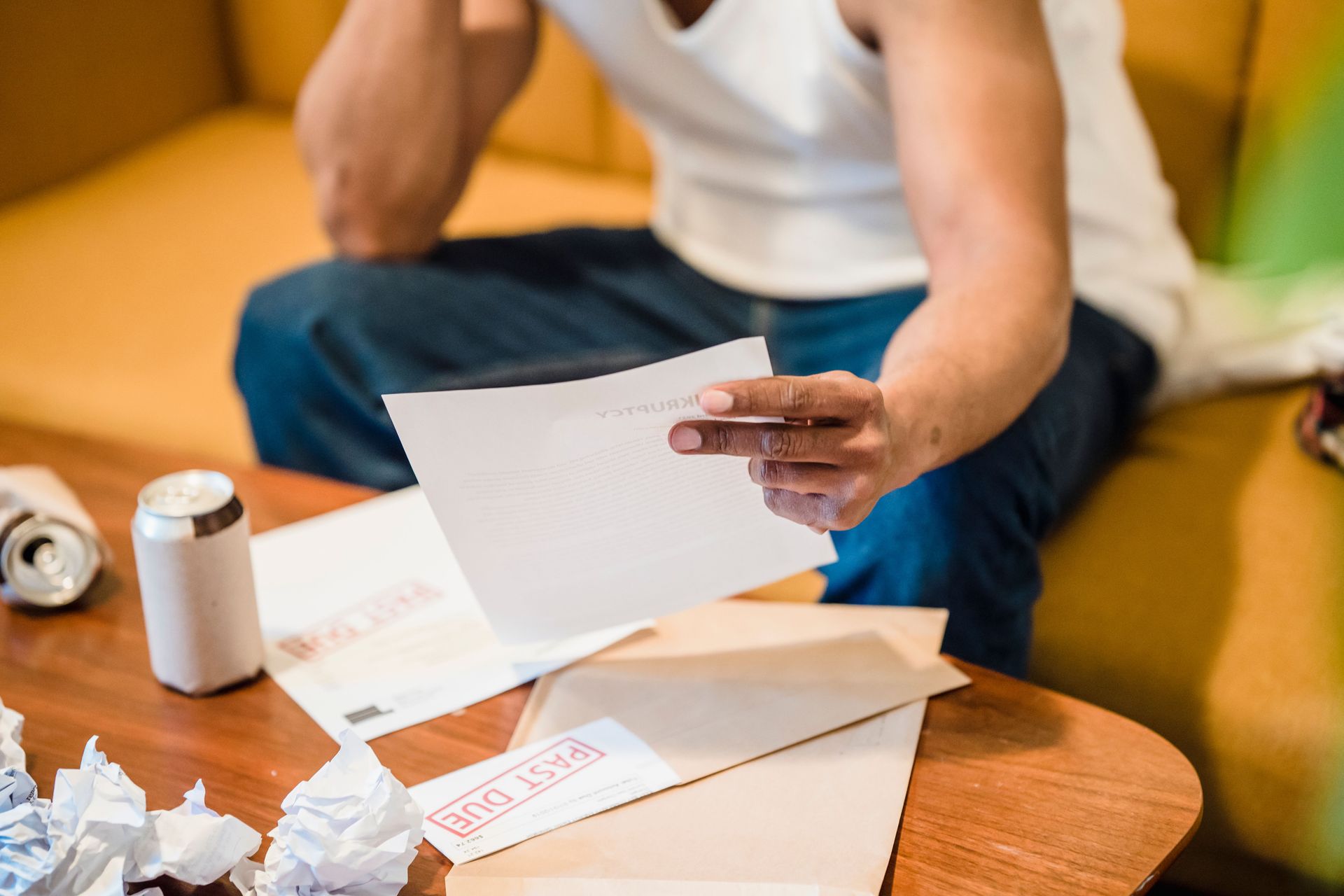Person sitting at a table reading a letter beside a soda can and crumpled papers
