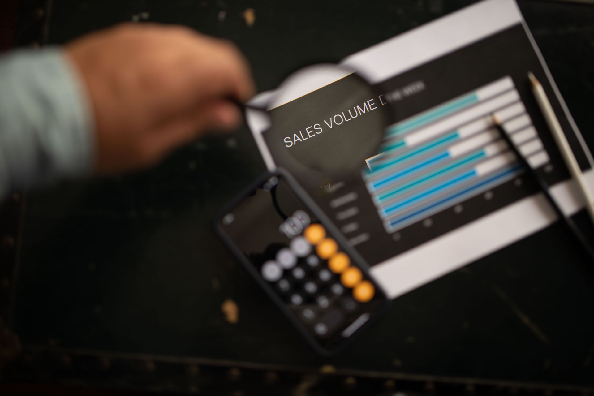 Hand holding a calculator beside a tablet showing a bar chart on a dark desk