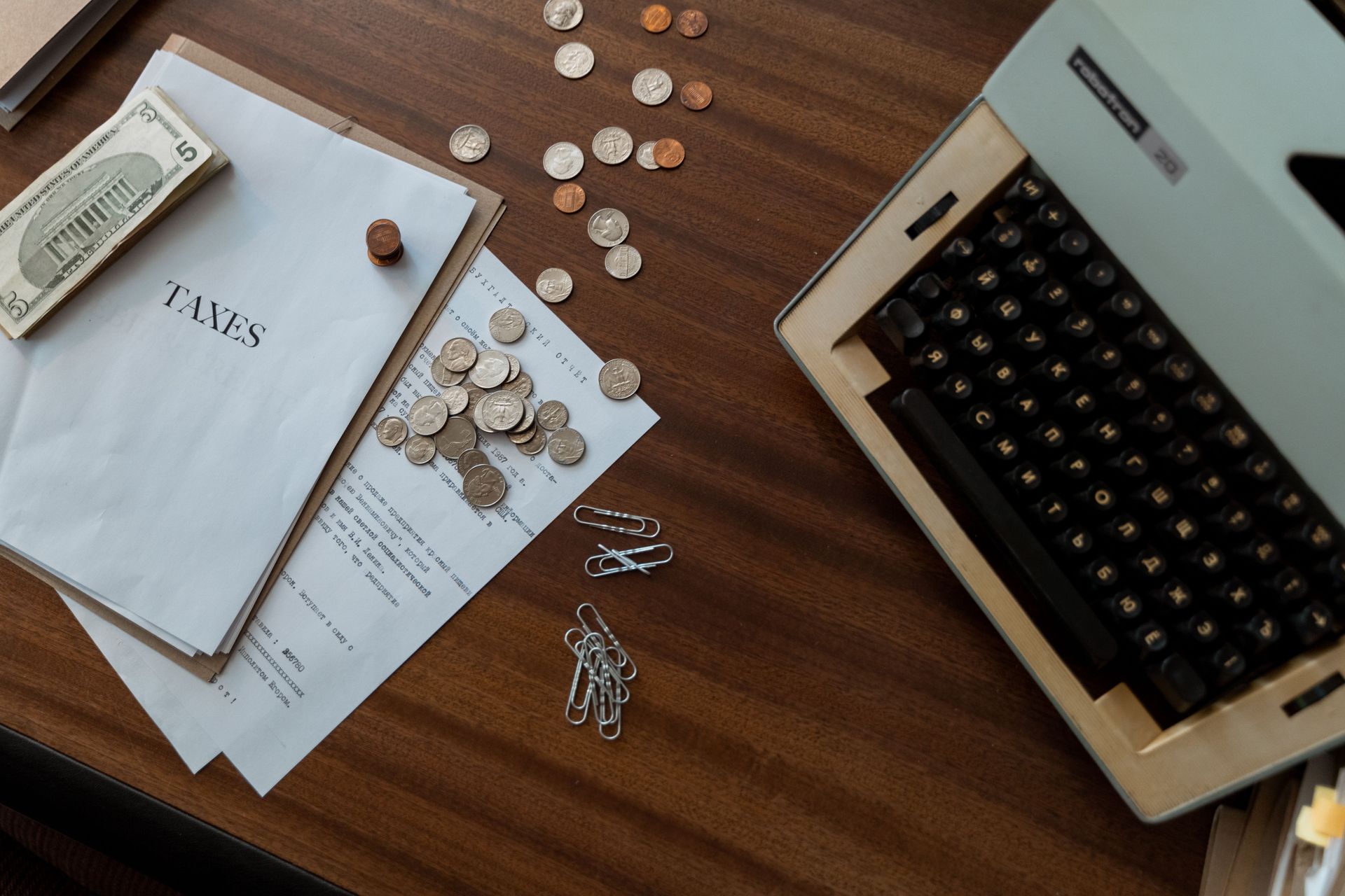 Aerial view of a wooden desk with a typewriter, papers, coins, and a stamp set.
