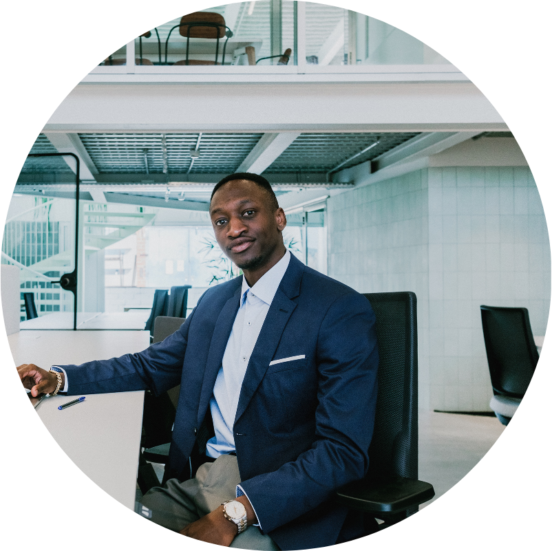 Black man in a blue blazer sits at a desk in a modern office, looking at the camera.