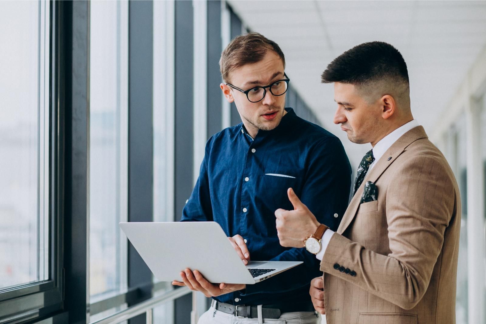 Two men are standing next to each other looking at a laptop.