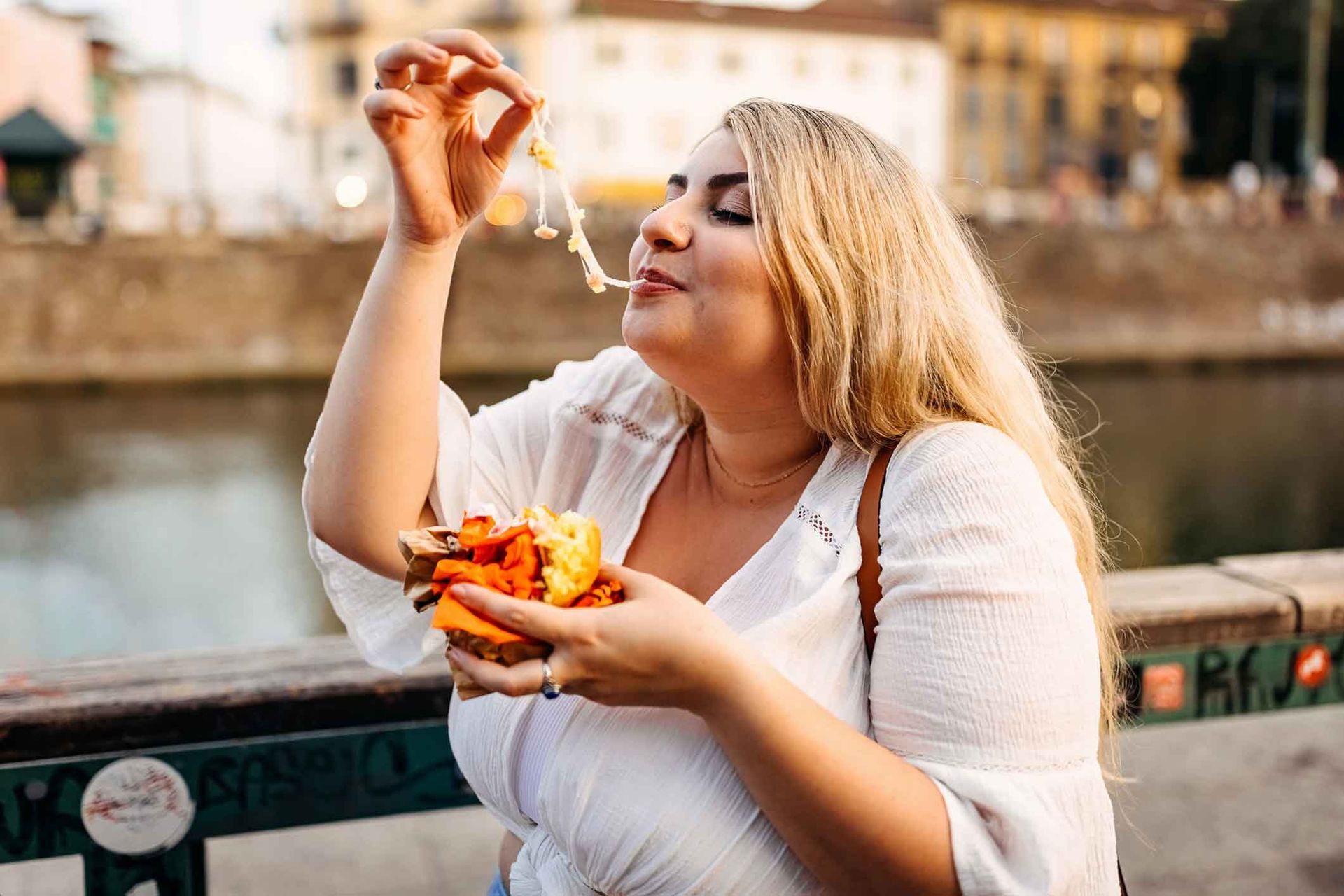 A woman is eating a hamburger on a bridge.