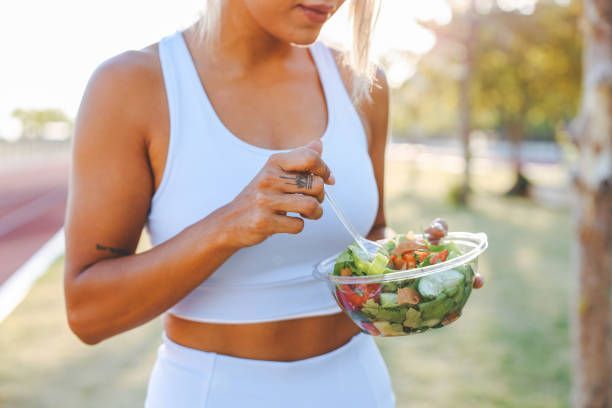 A woman is eating a salad with a fork in a park.