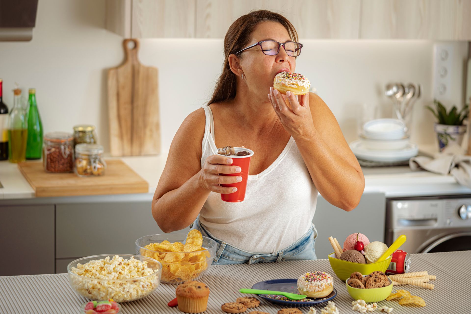 A woman is sitting at a table eating a cupcake and drinking soda.