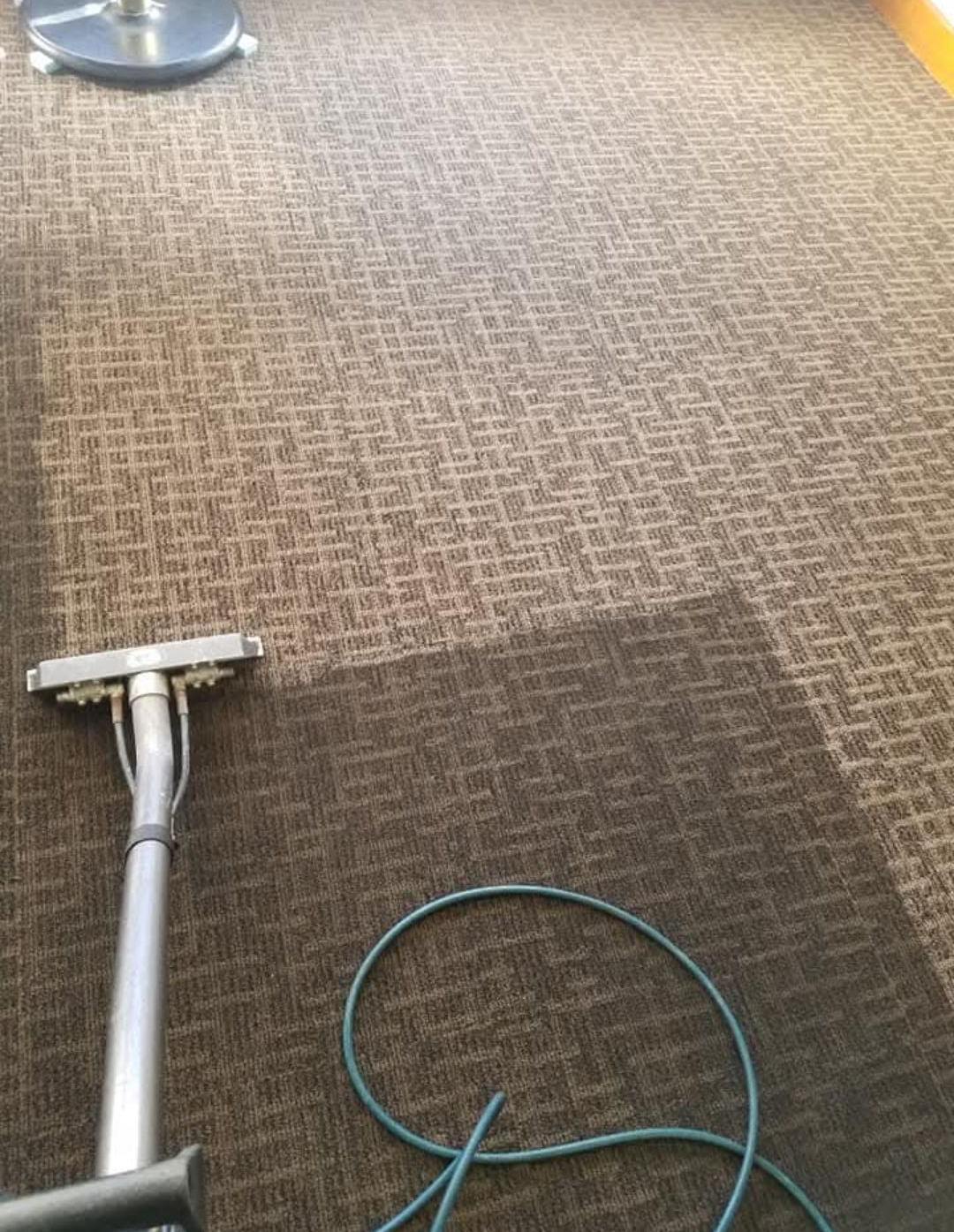 Person vacuuming a white rug in a living room. Tools lean against the wall near a dark sofa.