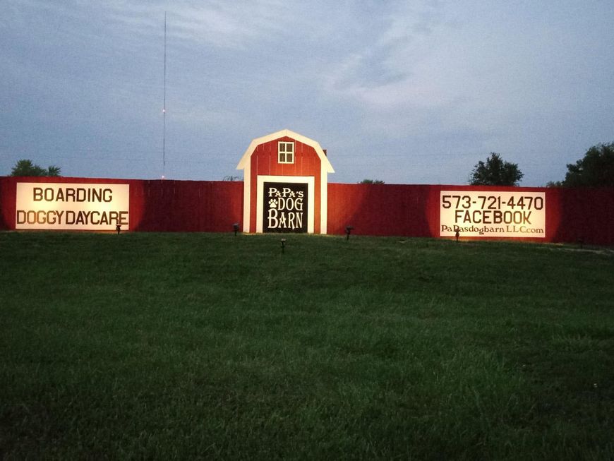 Red dog daycare building behind a green lawn and red fence with signs and phone number.
