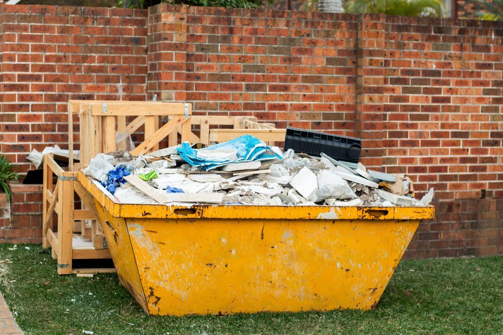 A Yellow Dumpster Filled With Trash Is Sitting In Front Of A Brick Wall — Green Solutions Qld in Mulara, QLD