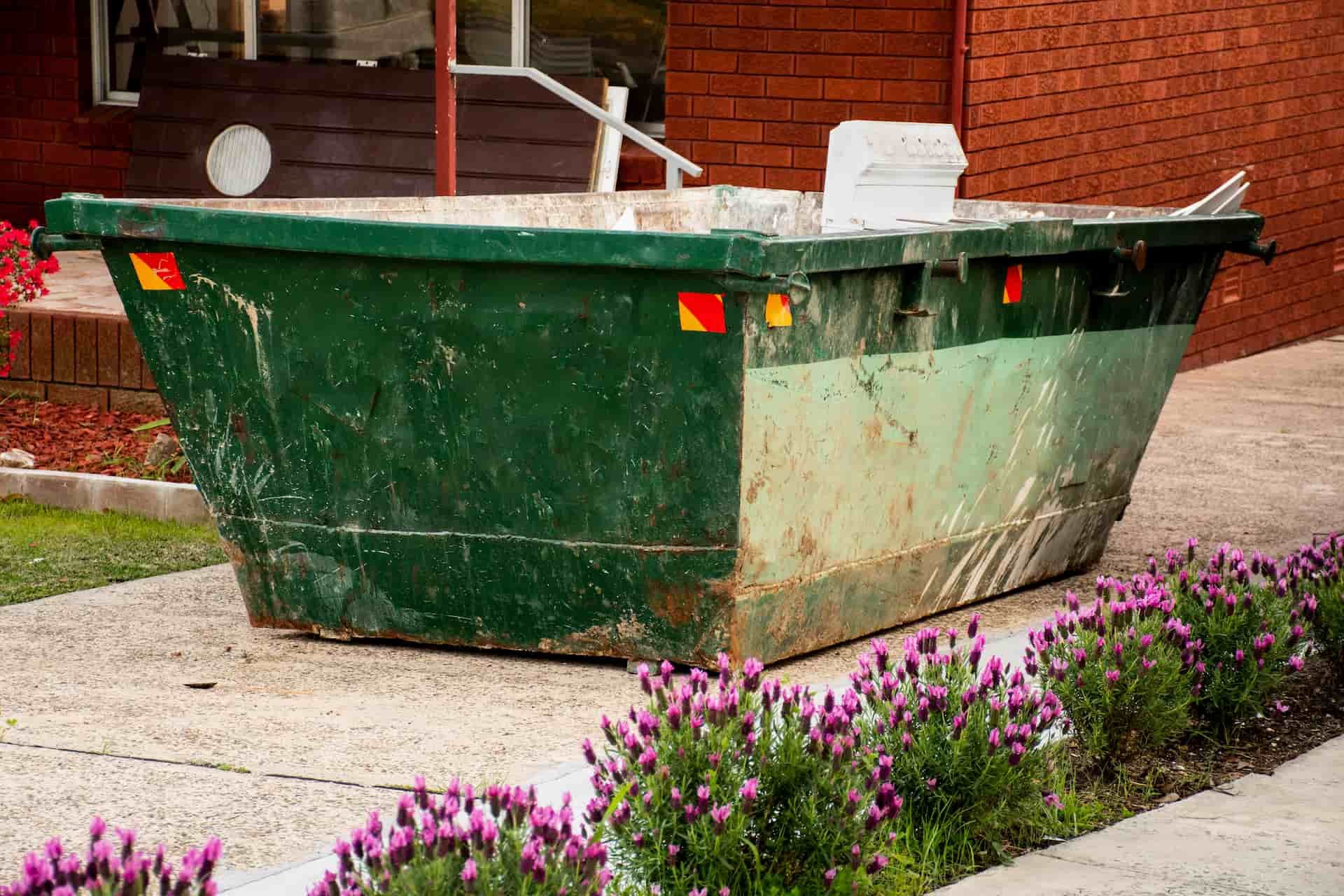 A Green Dumpster Is Sitting On The Sidewalk In Front Of A Brick Building — Green Solutions Qld in Mulara, QLD