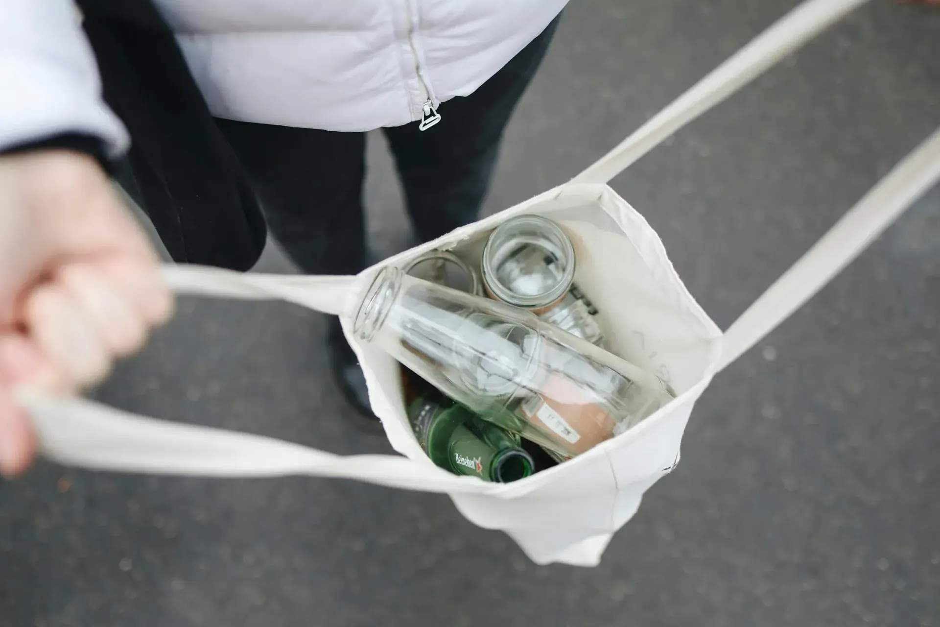 Person holding a white tote bag filled with glass bottles, possibly for recycling.