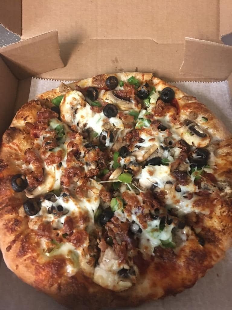 Open pizza in a cardboard box, topped with cheese, olives, and green peppers.