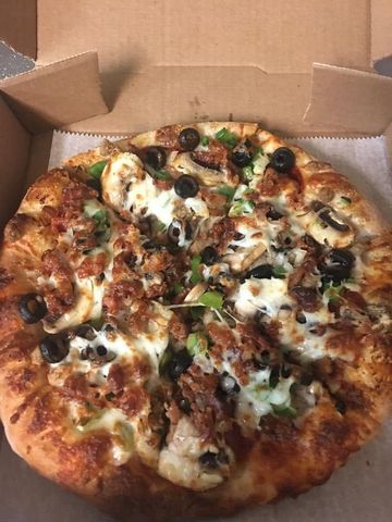 Open pizza in a cardboard box, topped with cheese, olives, and green peppers.
