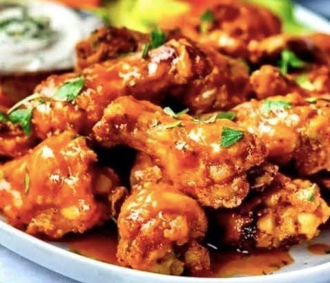 Close-up of crispy fried chicken wings coated in glossy orange sauce, garnished with parsley on a plate