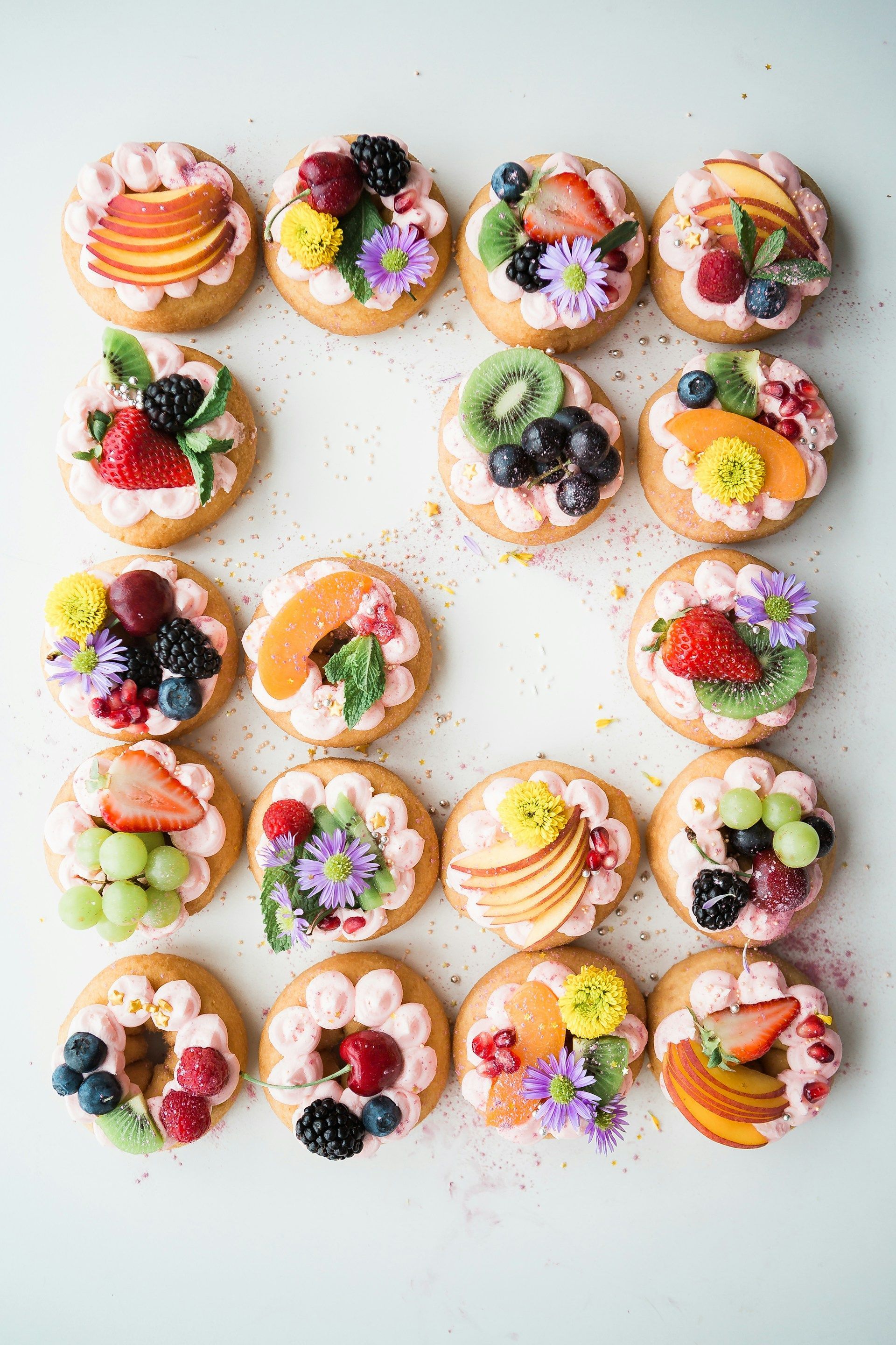 Assorted colorful mini fruit tarts arranged on a white surface