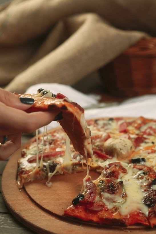 Hand lifting a cheesy slice of pizza from a wooden board with a blurred background
