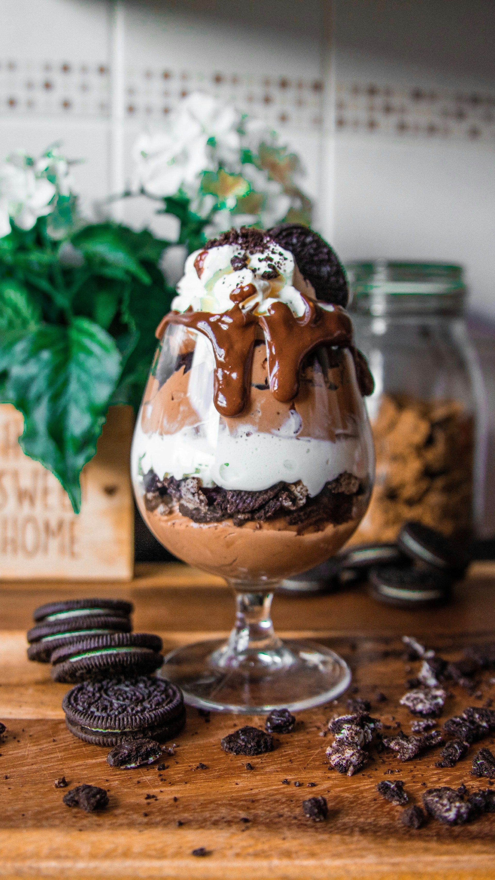 Chocolate ice cream sundae in a glass with Oreo cookies and chocolate drizzle on a wooden table.