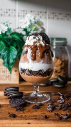 Chocolate ice cream sundae in a glass with Oreo cookies and chocolate drizzle on a wooden table.