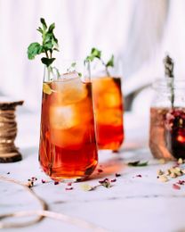 Two amber cocktails with mint and ice on a white table, with scattered flower petals