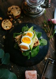 Open-faced egg sandwich on dark plate with greens, on a rustic wooden table