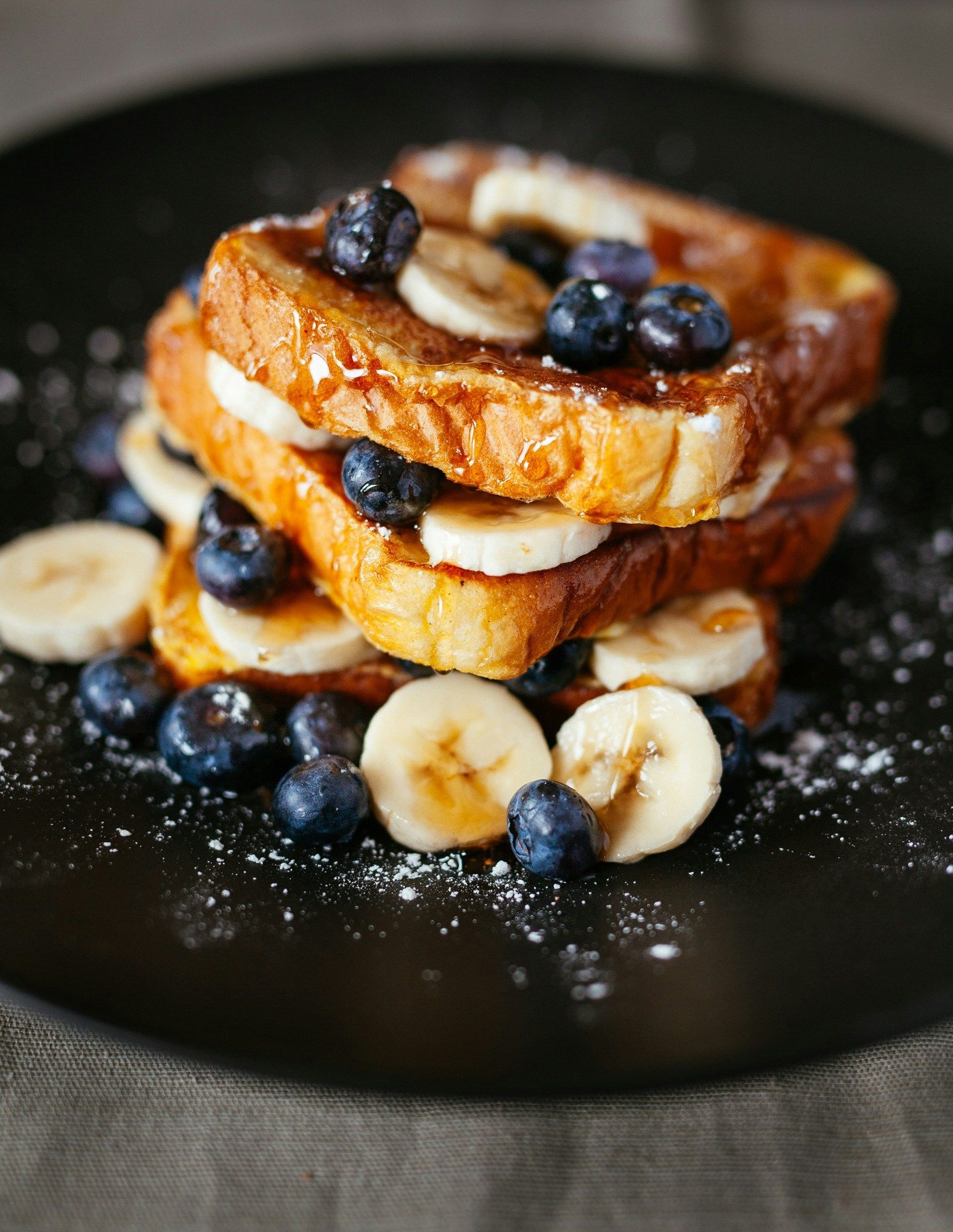 French toast stack topped with blueberries and banana slices on a dark plate