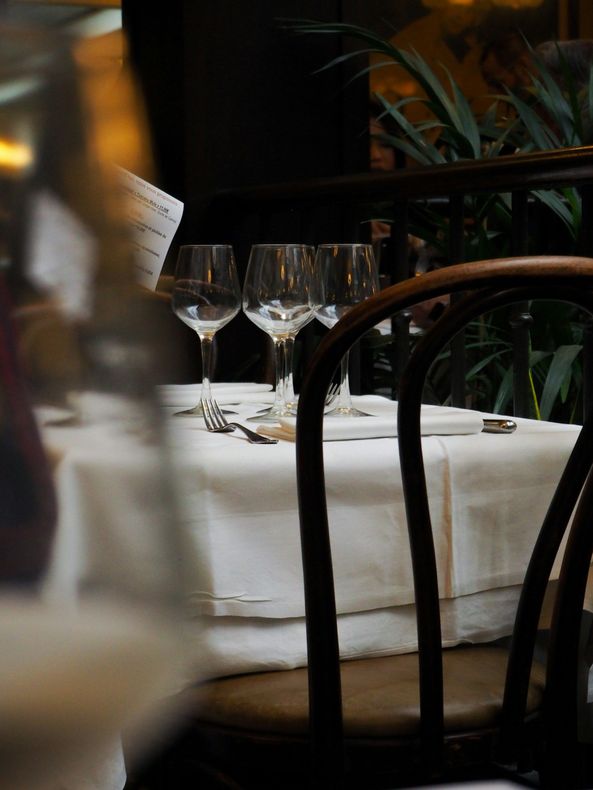 Dimly lit restaurant table with white tablecloth, wine glasses, and wooden chairs
