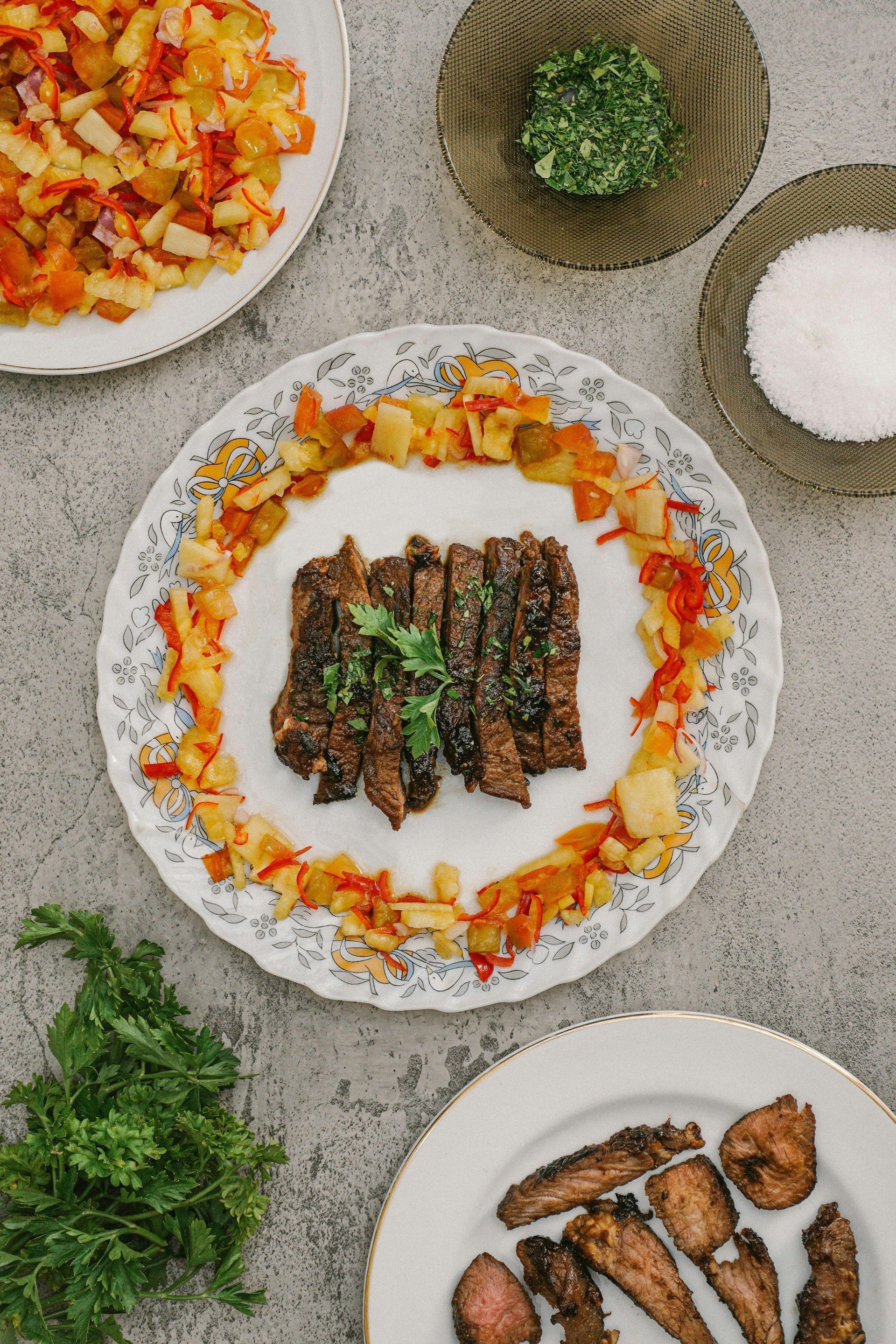 Overhead spread of plated grilled meat, chopped vegetables, herbs, and seasonings on a tabletop