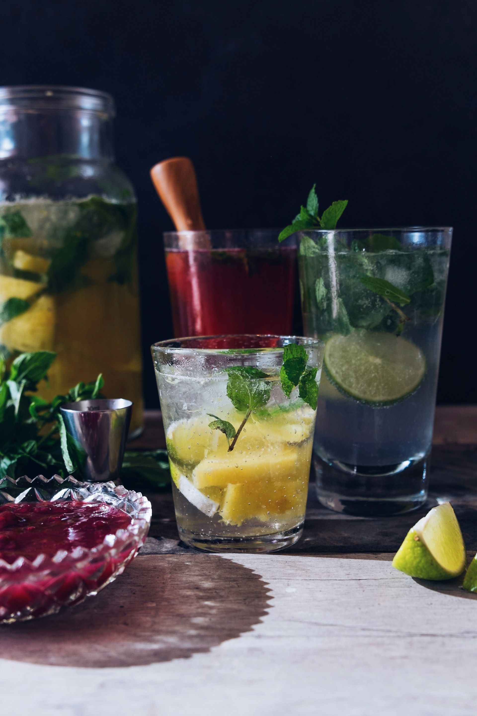 Mojito and fruit cocktails with lime and mint on a table, with a pitcher in the background