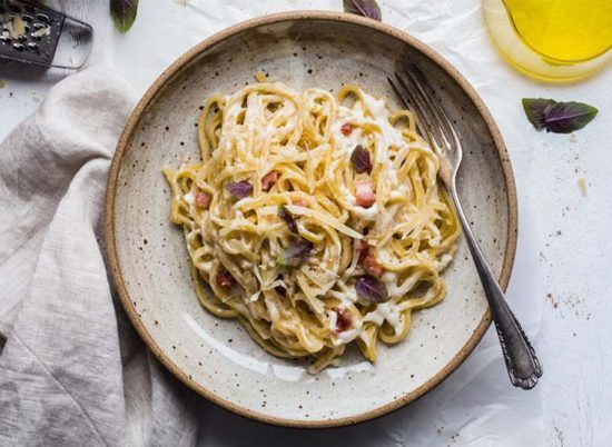 Creamy pasta with bacon in a rustic bowl on a light cloth, with a fork beside it.
