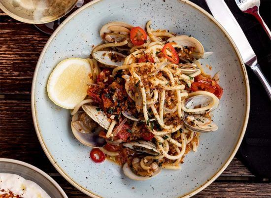 Plate of spaghetti with clams, red sauce, and lemon wedge on a rustic wooden table
