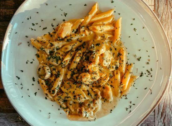 Pasta in creamy orange sauce on a white plate, sprinkled with herbs