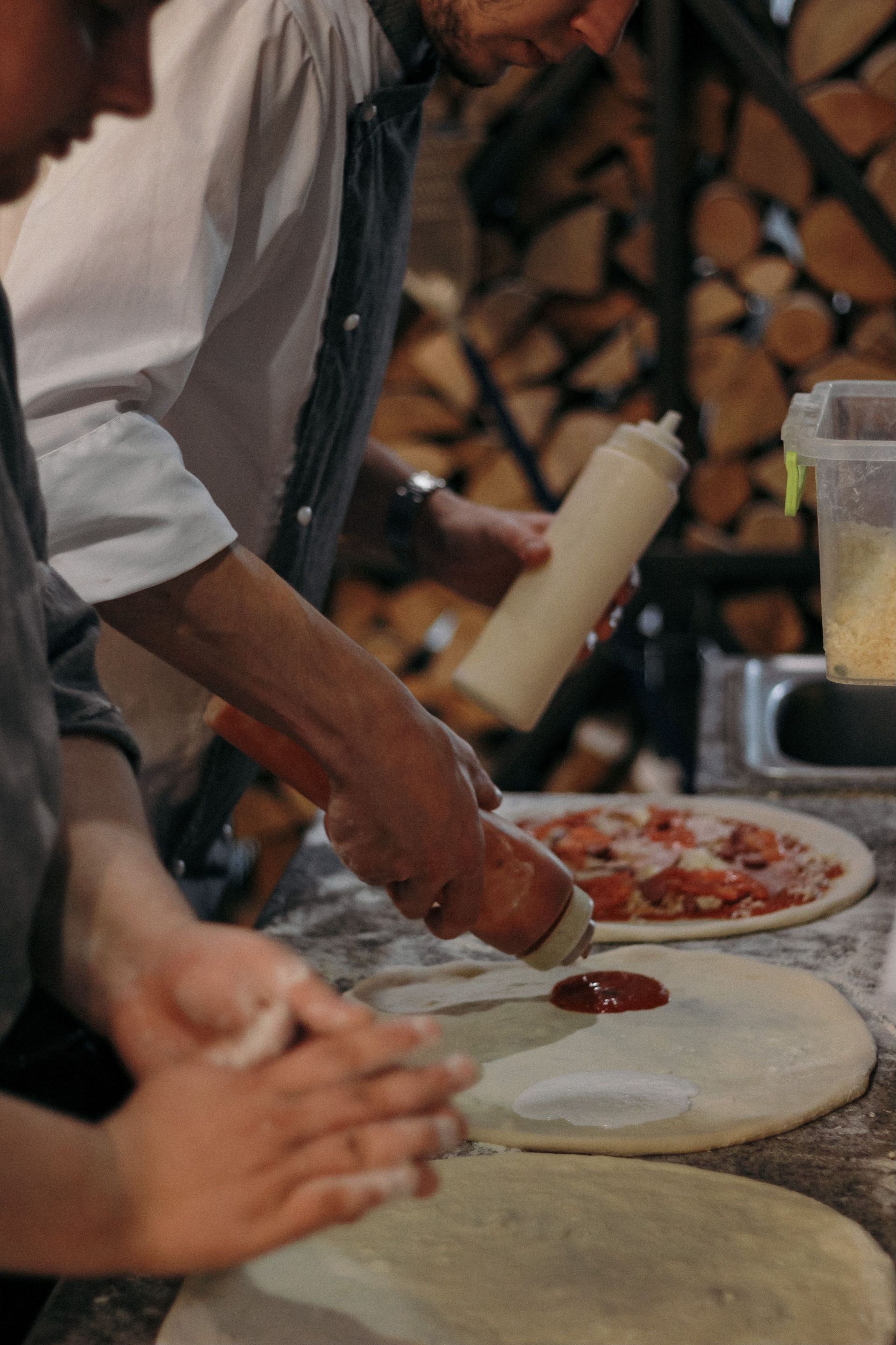 Chef spreading tomato sauce on pizza dough in a restaurant kitchen