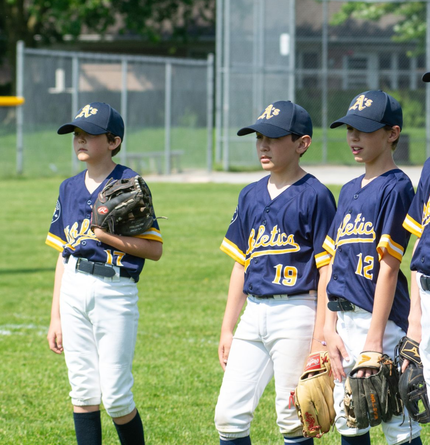 Youth baseball players in blue and gold uniforms, standing on a grassy field, wearing hats and holding gloves.