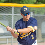 Man in baseball uniform swings bat at a ball, outdoors.