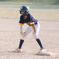 Youth baseball player in uniform at the plate, wearing a helmet, with hands on knees.
