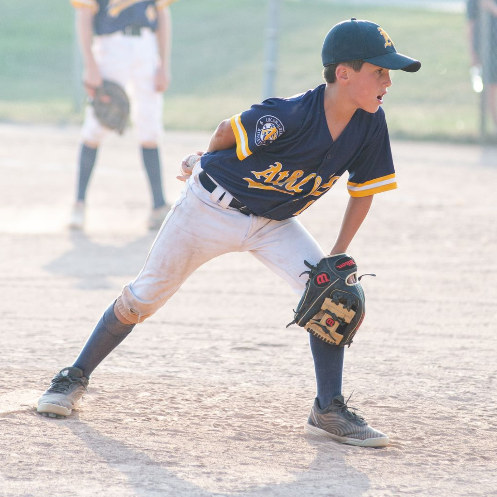 Young baseball player in a navy blue uniform throws a ball on a baseball field.
