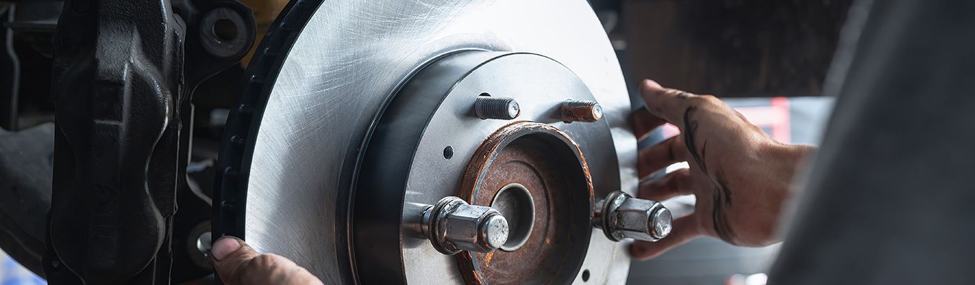 A person installs a silver metal brake rotor onto a vehicle wheel hub.