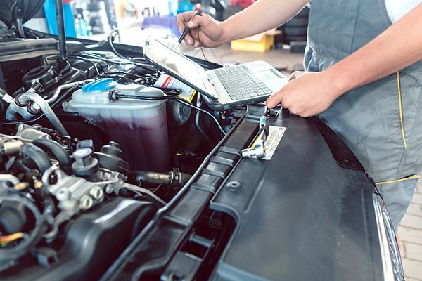 A man is working on the engine of a car with a laptop.