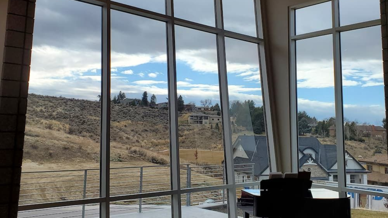 Large windows with grid patterns offer views of a cloudy sky and houses on a hillside.