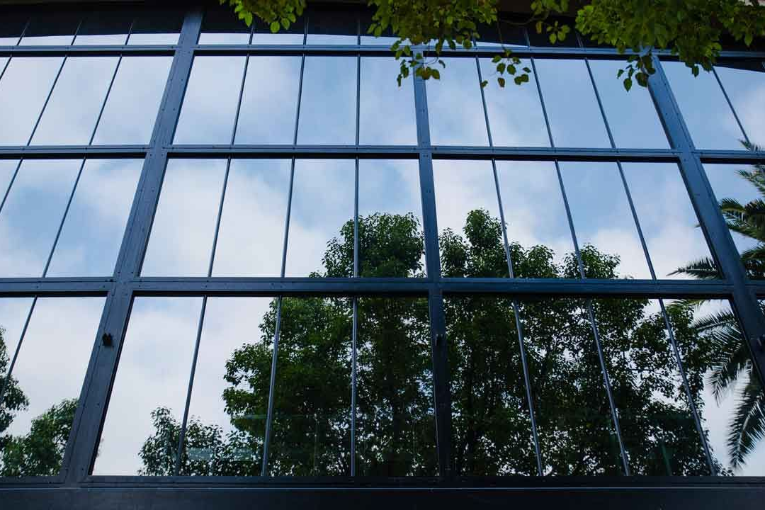 Blue glass facade of a modern building, reflecting the sky, with a curved shape and some visible windows.