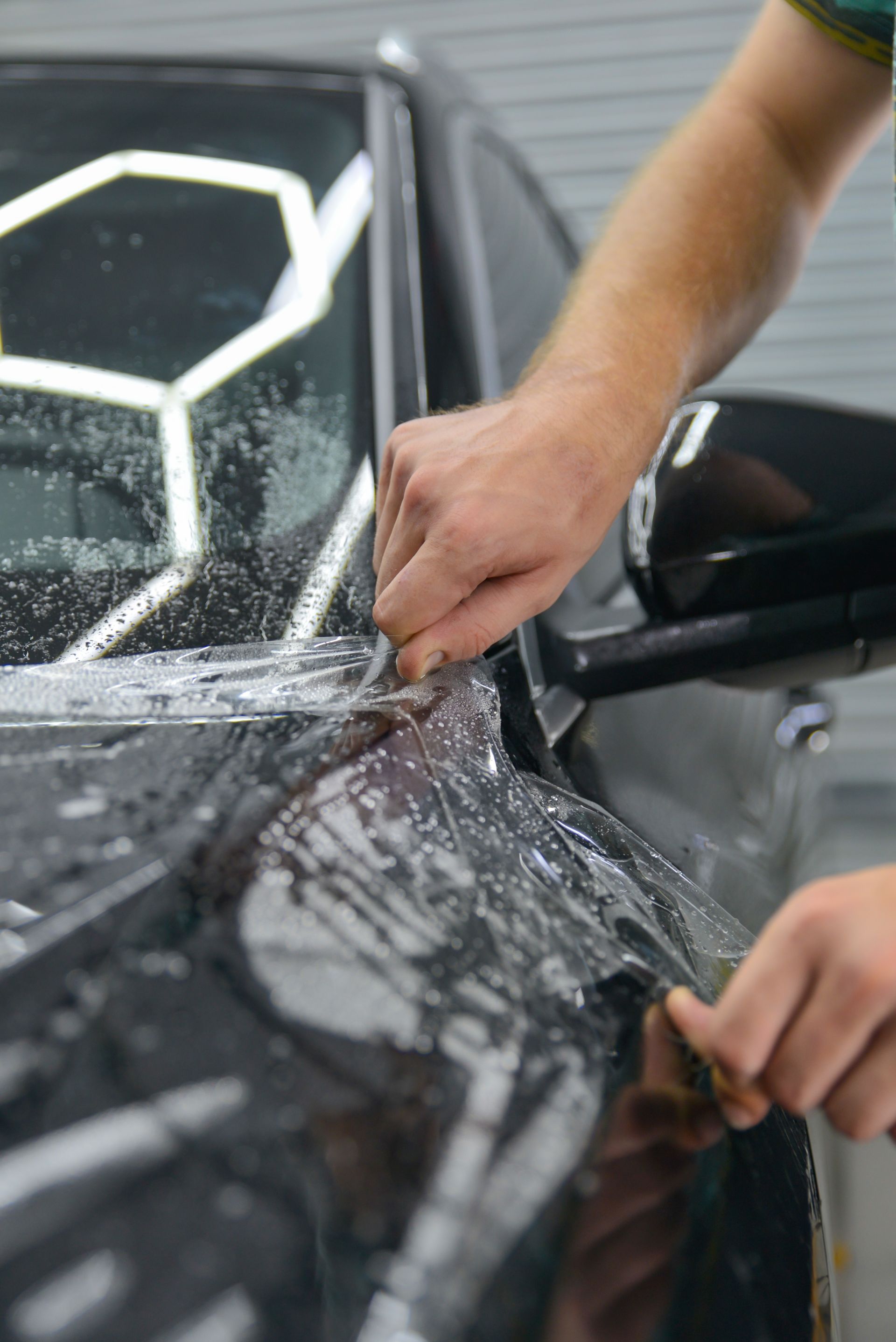 A person applying a blue polishing pad to a dark-colored car hood.