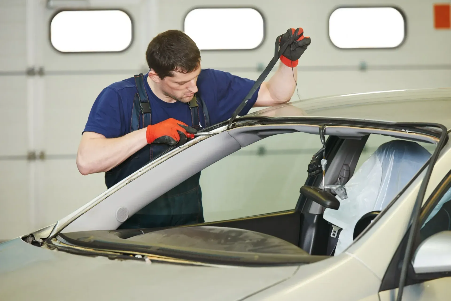 Mechanic in blue shirt and gloves replacing a windshield.