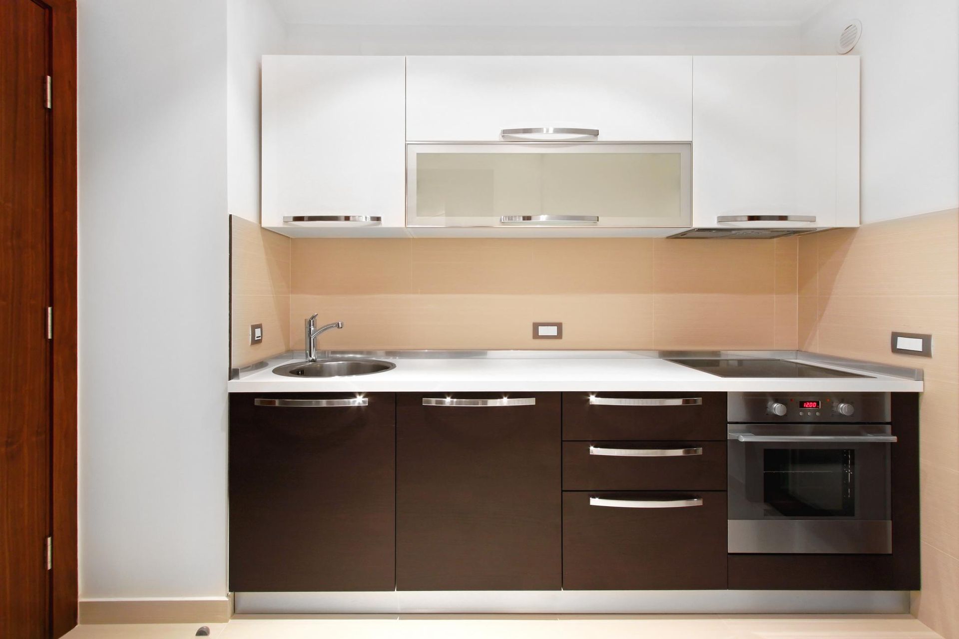 Modern kitchen with dark cabinets, white upper cabinets, sink, cooktop, and built-in oven.