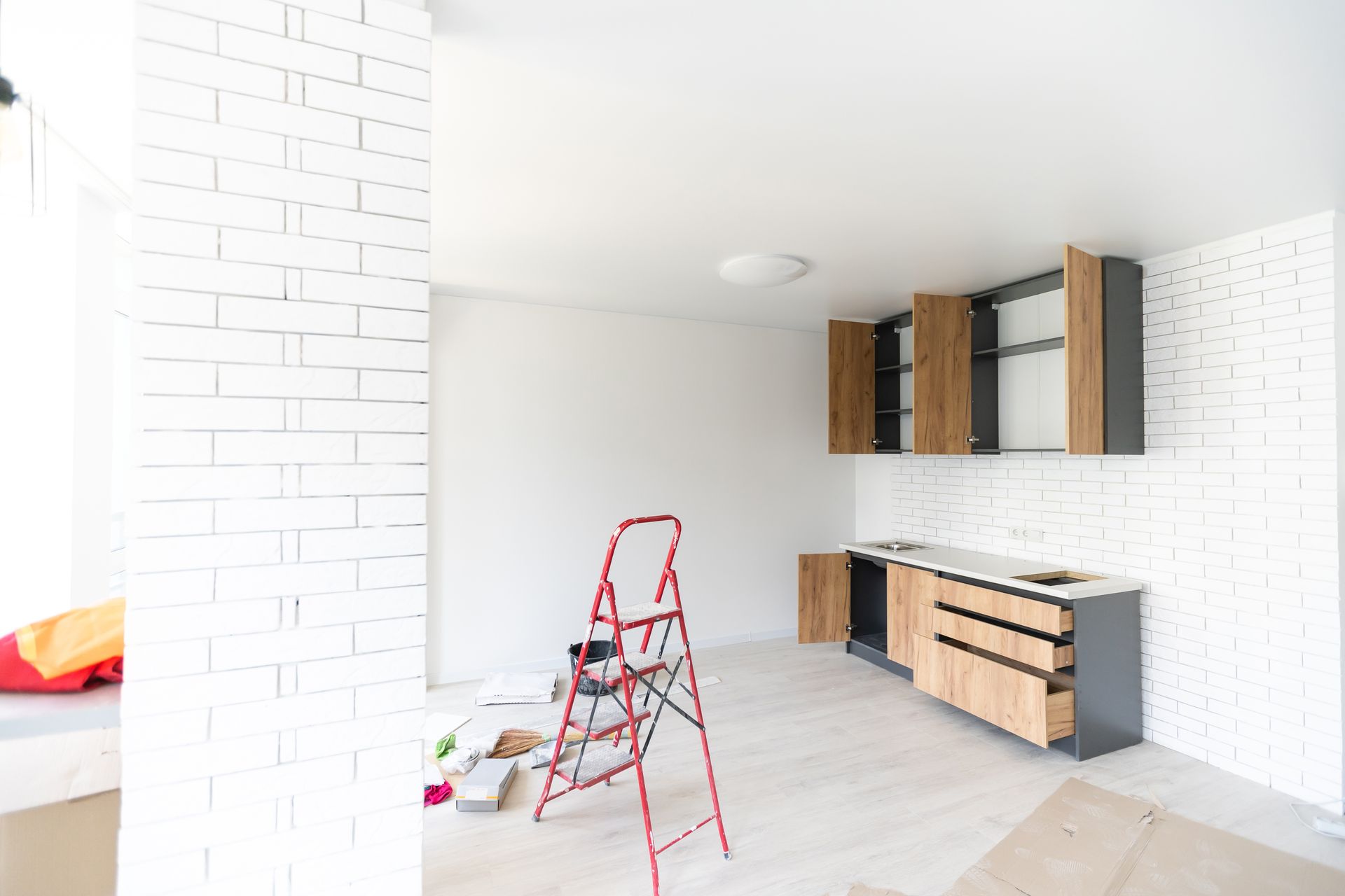 Bright unfinished kitchen with red step ladder and white brick walls