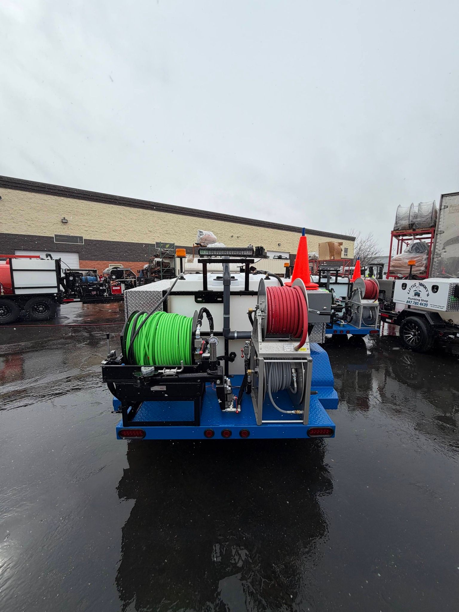 Blue utility trailer with green and red hose reels in a wet parking lot on a rainy day