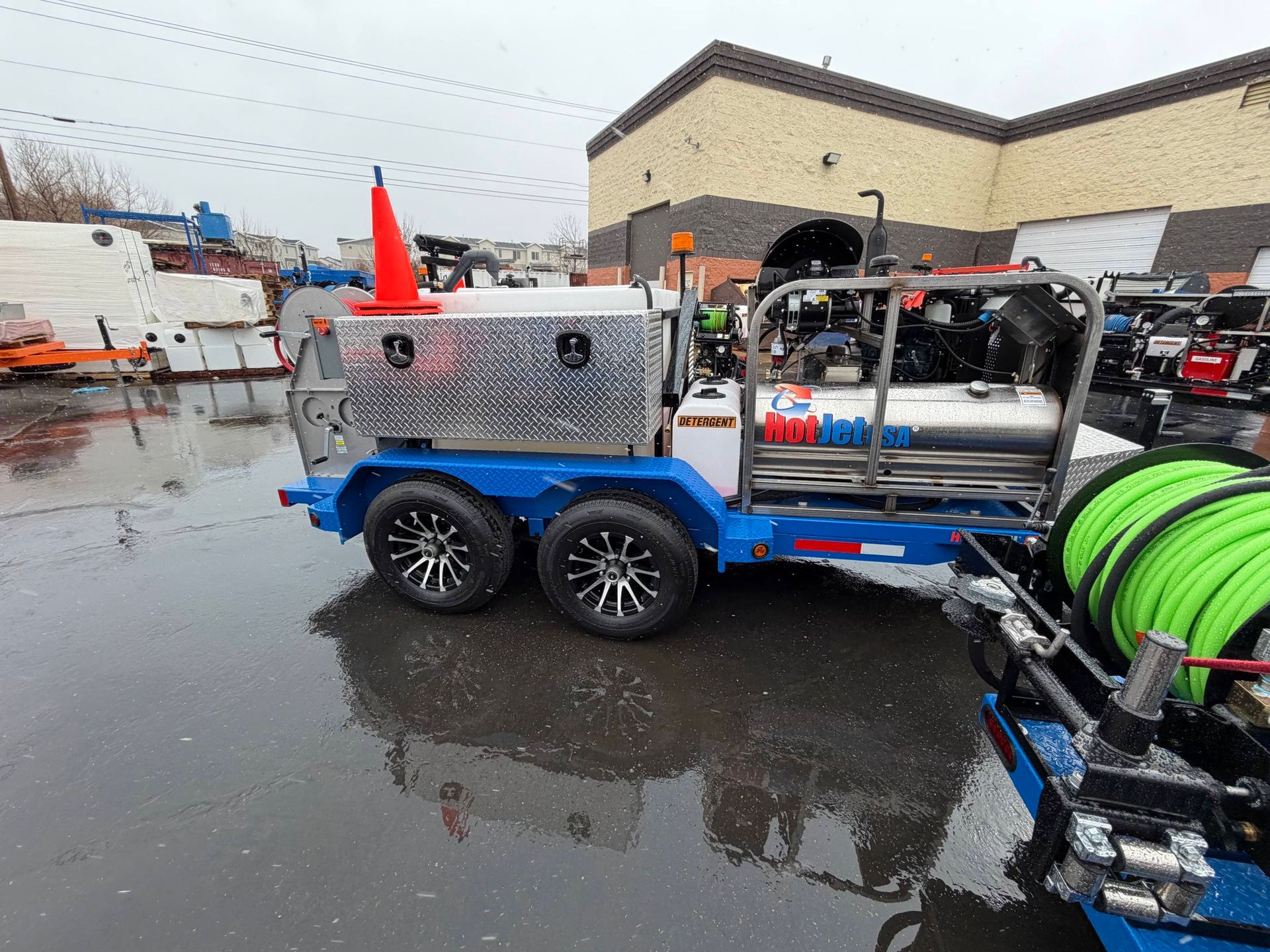Blue utility trailer with cones and hose reels in a wet parking lot outside a building
