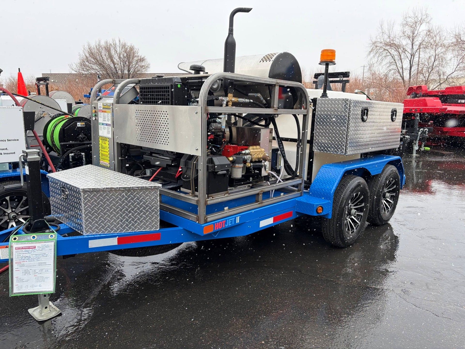 Blue trailer carrying a silver off-road utility vehicle in a rainy outdoor lot