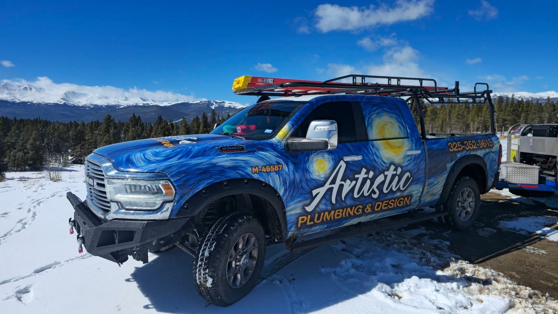 Blue Artistic Plumbing service truck parked in snowy landscape with mountains in the background