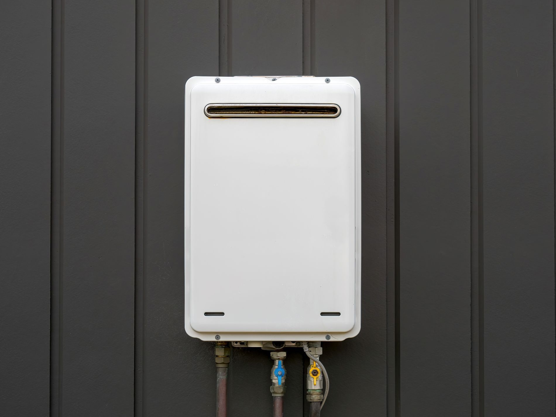 White wall-mounted gas water heater with pipes and valves against a dark gray wall