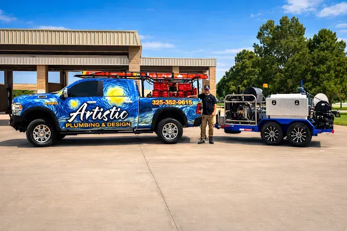 Blue “Artistic” truck towing a white trailer, with a person standing beside it in a sunny parking lot.