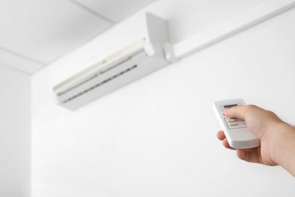 Mano che impugna un telecomando puntato verso un condizionatore d'aria a parete