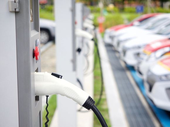 Prese di ricarica per auto elettriche collegate presso una stazione di ricarica, con auto parcheggiate sullo sfondo.